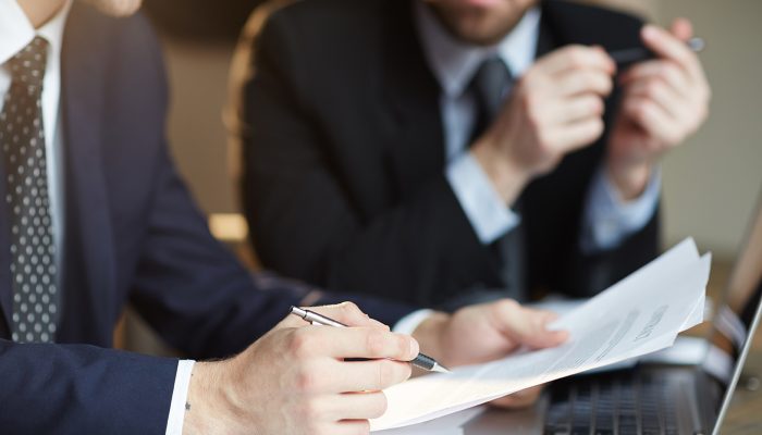 Closeup portrait of two unrecognizable  business partners reviewing paperwork and signing contract papers at table during meeting